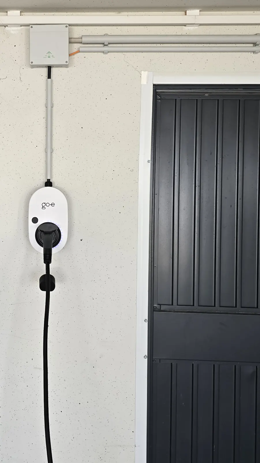 Weiße Wallbox mit Ladekabel an einer hellen Garagenwand