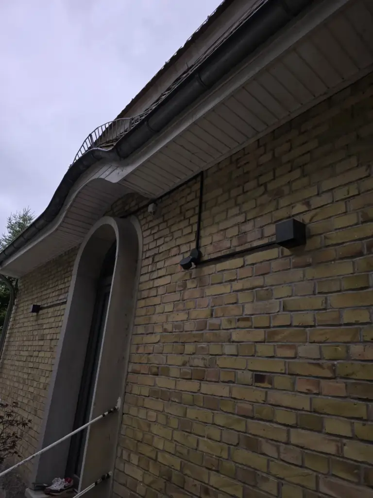 Außen an einer Klinkerfassade verlegte Leitung mit Anschlussdose unter dem Dachüberstand